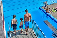 Ein Mann und zwei Jungen sind auf der Plattform eines Abspringturms im Freibad zu sehen