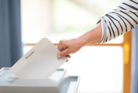 Eine Hand wirft einen Stimmzettel in eine Wahlurne