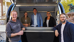 Außenaufnahme mit (von links) Marktmeister Jens Berghahn, Ann-Christin Lüersen (Gilde Wirtschaftsförderung), Bürgermeister Frank Hilker, Sabine Rosner (Zukunftsmanagerin Innenstadt) sowie Andreas Busch (stellvertretender Marktmeister) vor und in dem neuen Verkaufsanhänger