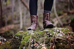 Beine in braunen Schnürstiefeln im Vintage-Look mit seitlichen Reißverschlüssen, die auf einem moosbedeckten Stein stehen