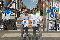 Außenaufnahme von (links nach rechts) Christian Schmidt (Vorsitzender der Werbegemeinschaft „Die Händler“) und Bürgermeister Frank Hilker an der Kreuzung Lange Straße Krumme Straße, zudem sind noch zwei Bilder (rechts und links im Bild) der Straßenschilder in der Krummen Straße (links) und in der Exterstraße / Langen Straße zu sehen
