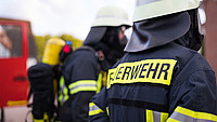 Drei Personen in Feuerwehr-Uniform stehen in einer Reihe mit dem Rücken zur Kamera