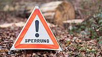 Warndreieck auf Waldboden mit der Aufschrift "SPERRUNG" und einem Ausrufezeichensymbol darüber