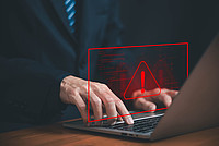 Hände, die auf einer Laptop-Tastatur tippen und darüber ein Warnzeichen und unscharfer Programmier-Code in rot