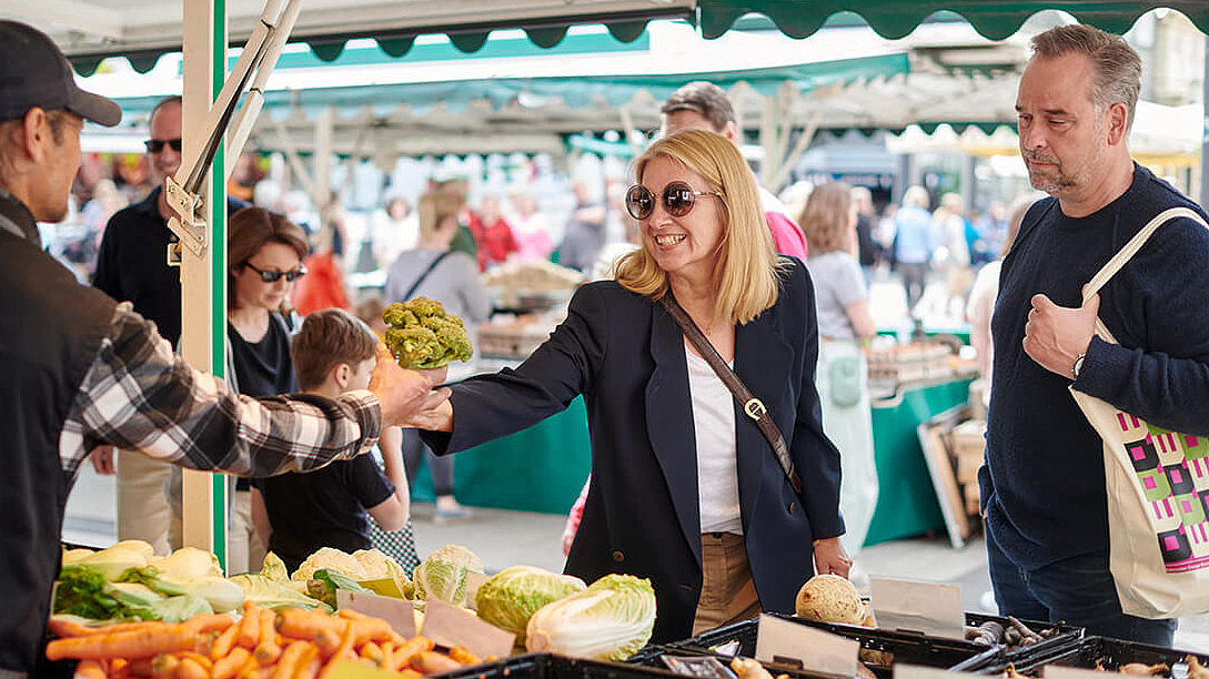 Eine Frau nimmt einen Strauß Gemüse bei einem Händler auf dem Wochenmarkt entgegen