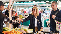 Eine Frau nimmt einen Strauß Gemüse bei einem Händler auf dem Wochenmarkt entgegen