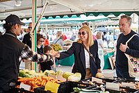 Eine Frau nimmt einen Strauß Gemüse bei einem Händler auf dem Wochenmarkt entgegen