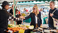 Eine Frau nimmt einen Strauß Gemüse bei einem Händler auf dem Wochenmarkt entgegen