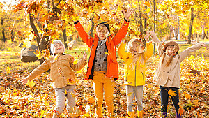 Vier Kinder spielen bei herbstlicher Stimmung im Park mit Laub