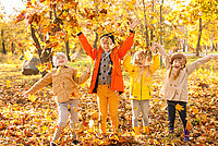 Vier Kinder spielen bei herbstlicher Stimmung im Park mit Laub