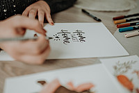 Hände schreiben im Handlettering-Stil den Schriftzug "Home Sweet Home" auf ein Stück Papier