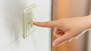 Eine Hand betätigt einen Lichtschalter mit dem Zeigefinger