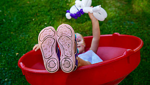 Ein Mädchen liegt in einem roten Outdoor-Spielzeug-Trichter und streckt die rosa Schuhsohlen Richtung Kamera