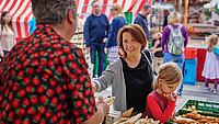 Ein Händler reicht einer Frau auf dem Wochenmarkt Spargel