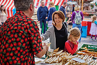 Ein Händler reicht einer Frau auf dem Wochenmarkt Spargel