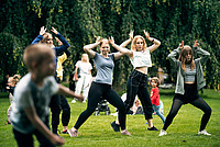 Mehrere Frauen machen Sportübungen in einem Park, im Vordergrund ist unscharf ein kleiner Junge zu sehen