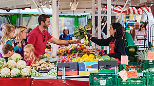Eine Marktbeschickerin überreicht einem Mann auf dem Wochenmarkt in Detmold Gemüse