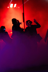 Schwarze Silhouetten von tanzenden Personen vor einer rot beleuchteten Kulisse