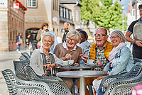 Eine Gruppe von vier Rentnerinnen und Rentnern sitzt draußen an einem Tisch in der Detmolder Innenstadt und schaut sich gemeinsam lachend etwas an