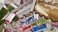 Außenaufnahme eines Karussells in Detmold auf einer Kirmes, welches sich dreht. In den einzelnen Abteilen des Karussells sind Fahrgäste zu sehen.
