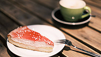 Ein Stück Kuchen auf einem weißen Teller neben einer grünen Kaffeetasse auf einem Holztisch