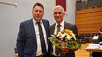 Fotografie von Bürgermeister Frank Hilker (links) mit dem neuen Beigeordneten der Stadt Detmold, Thorsten Paulussen (rechts), welcher einen Blumenstrauß in den Händen hält