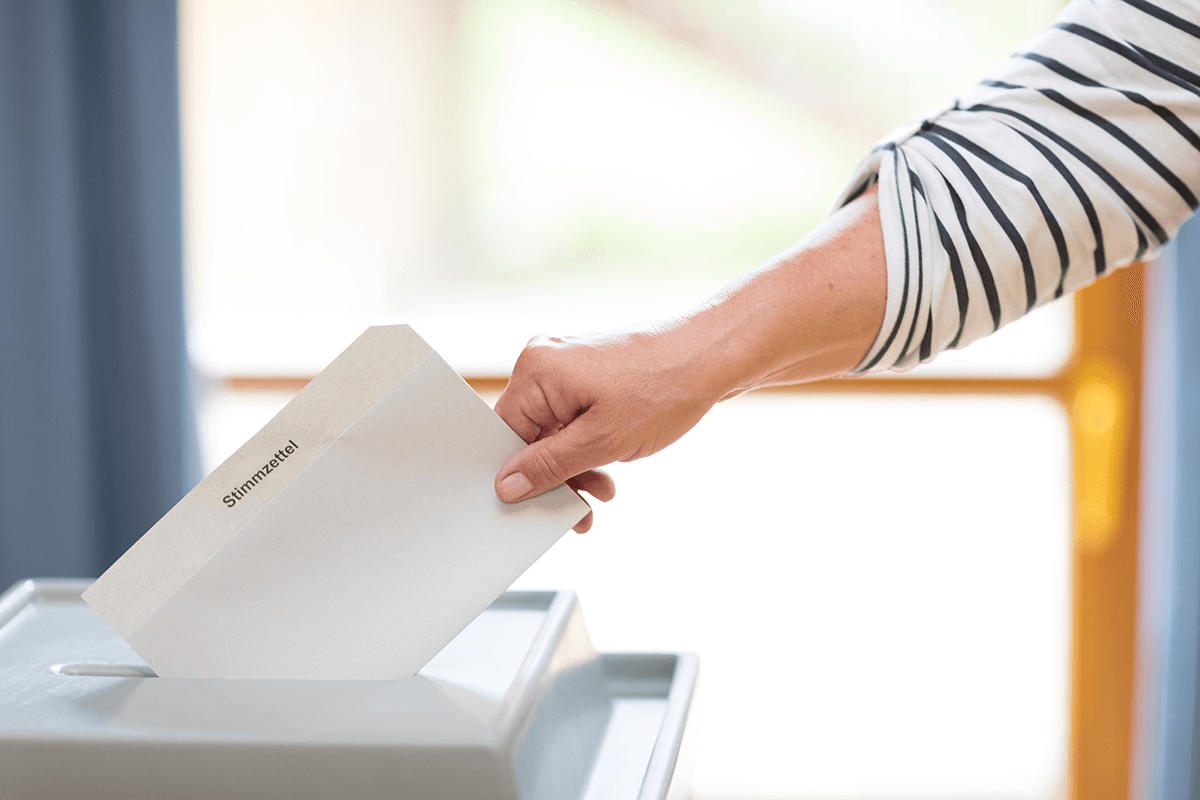 Eine Hand wirft einen Stimmzettel in eine Wahlurne