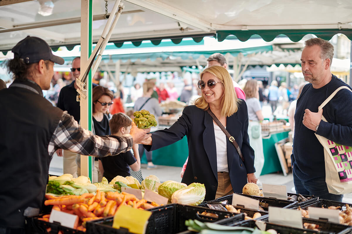 Eine Frau nimmt einen Strauß Gemüse bei einem Händler auf dem Wochenmarkt entgegen