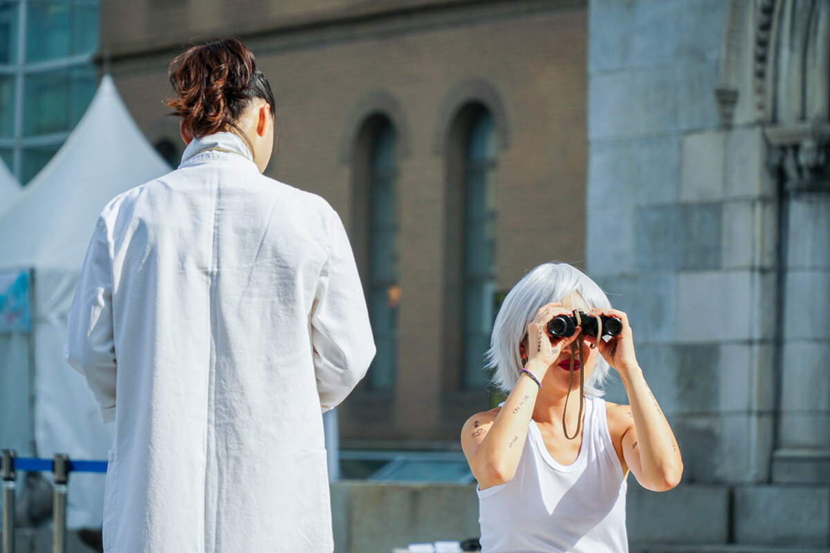 Die koreanische Künstlerin Jiin Gook mit einem Fernglas in der Hand bei einer ihrer Performances