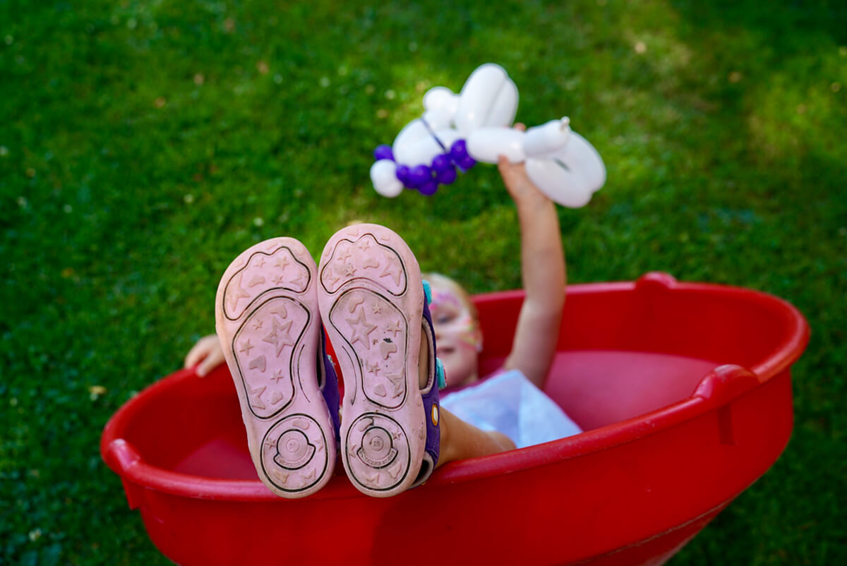 Ein Mädchen liegt in einem roten Outdoor-Spielzeug-Trichter und streckt die rosa Schuhsohlen Richtung Kamera