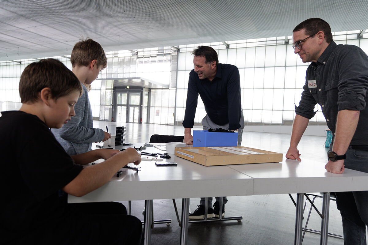 Bürgermeister Frank Hilker und Michael Koch (Fachbereich 2) an einem Tisch mit mehreren Kinder während der LEGO-Bauaktion im Hangar 21