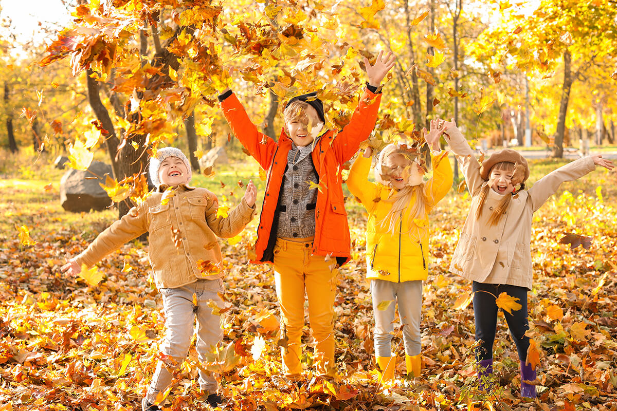 Vier Kinder spielen bei herbstlicher Stimmung im Park mit Laub