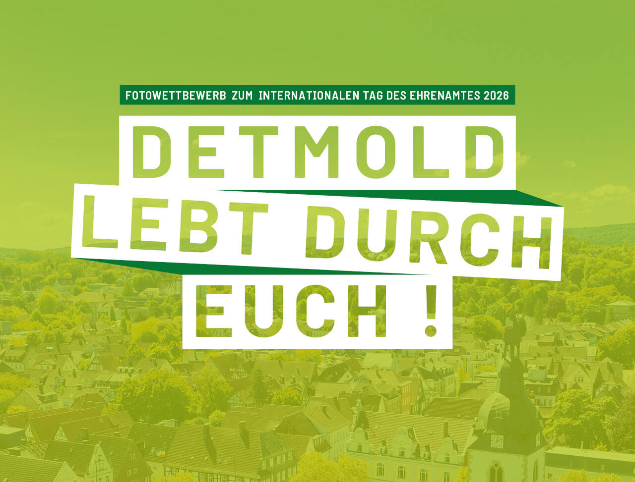 Luftaufnahme über Detmold mit einem hellgrünen Overlay und den Worten "Detmold lebt durch euch!" und "Fotowettbewerb zum internationalen Tag des Ehrenamtes 2026" darauf